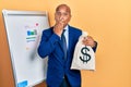 Middle age latin man wearing business suit holding dollars bag covering mouth with hand, shocked and afraid for mistake Royalty Free Stock Photo