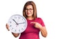 Middle age latin woman holding big clock smiling happy pointing with hand and finger