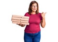 Middle age latin woman holding delivery pizza box pointing thumb up to the side smiling happy with open mouth Royalty Free Stock Photo