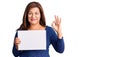 Middle age latin woman holding paper banner with blank space doing ok sign with fingers, smiling friendly gesturing excellent Royalty Free Stock Photo