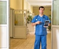 Middle age male doctor in blue scrubs holding and pointing to tablet with Health Insurance text