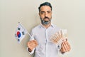 Middle age man with beard and grey hair holding south korea flag and won banknotes puffing cheeks with funny face Royalty Free Stock Photo