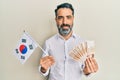 Middle age man with beard and grey hair holding south korea flag and won banknotes smiling with a happy and cool smile on face Royalty Free Stock Photo