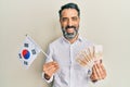 Middle age man with beard and grey hair holding south korea flag and won banknotes smiling and laughing hard out loud because Royalty Free Stock Photo