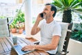Middle age man with beard smiling happy at the terrace working from home using laptop speaking on the phone Royalty Free Stock Photo