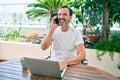 Middle age man with beard smiling happy at the terrace working from home using laptop speaking on the phone Royalty Free Stock Photo