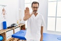 Middle age man with beard working at pain recovery clinic doing stop sing with palm of the hand Royalty Free Stock Photo