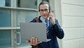 Middle age man business worker using laptop talking on smartphone at street Royalty Free Stock Photo