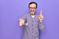 Middle age man changing tv channel using television remote control over purple background smiling with an idea or question Royalty Free Stock Photo