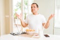 Middle age man eating asian food with chopsticks at home clueless and confused expression with arms and hands raised Royalty Free Stock Photo