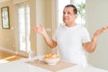 Middle age man eating rice at home clueless and confused expression with arms and hands raised Royalty Free Stock Photo