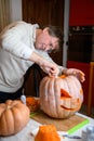 A middle age man, father, carving big orange pumpkin into jack-o-lantern for Halloween holiday decoration at kitchen Royalty Free Stock Photo