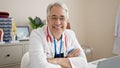 Middle age man with grey hair doctor smiling confident with arms crossed at clinic