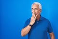 Middle age man with grey hair standing over blue background bored yawning tired covering mouth with hand Royalty Free Stock Photo