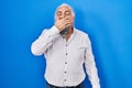 Middle age man with grey hair standing over blue background bored yawning tired covering mouth with hand Royalty Free Stock Photo