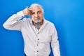 Middle age man with grey hair standing over blue background pointing unhappy to pimple on forehead, ugly infection of blackhead Royalty Free Stock Photo