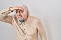 Middle age man with grey hair standing over isolated background very happy and smiling looking far away with hand over head Royalty Free Stock Photo