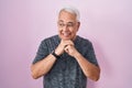 Middle age man with grey hair standing over pink background laughing nervous and excited with hands on chin looking to the side Royalty Free Stock Photo