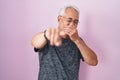 Middle age man with grey hair standing over pink background laughing at you, pointing finger to the camera with hand over mouth, Royalty Free Stock Photo