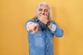 Middle age man with grey hair standing over yellow background laughing at you, pointing finger to the camera with hand over mouth, Royalty Free Stock Photo