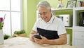 Middle age man with grey hair using smartphone sitting on the table at dinning room Royalty Free Stock Photo