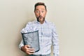 Middle age man holding paper bin full of crumpled papers scared and amazed with open mouth for surprise, disbelief face Royalty Free Stock Photo