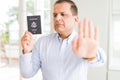 Middle age man holding holding passport of United States with open hand doing stop sign with serious and confident expression, Royalty Free Stock Photo