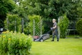 Middle age man mowing grass with electric lawn mower in a backyard. Gardening care tools and equipment. Process of lawn trimming Royalty Free Stock Photo