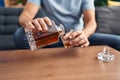 Middle age man pouring whisky on glass sitting on sofa at home Royalty Free Stock Photo