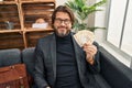 Middle age man psychologist holding denmark krone banknotes at psychology clinic