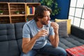 Middle age man taking pill drinking water sitting on sofa at home Royalty Free Stock Photo