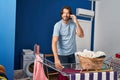 Middle age man talking on smartphone hanging clothes on clothesline at laundry room