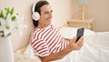 Middle age man using smartphone sitting on the bed wearing headphones at bedroom Royalty Free Stock Photo