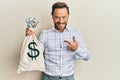 Middle age man wearing business shirt holding dollars bag pointing finger to one self smiling happy and proud Royalty Free Stock Photo