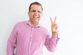 Middle age man wearing business shirt over white wall smiling with happy face winking at the camera doing victory sign Royalty Free Stock Photo
