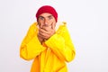 Middle age man wearing rain coat and woolen hat standing over isolated white background shocked covering mouth with hands for Royalty Free Stock Photo