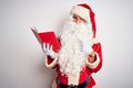 Middle age man wearing Santa Claus costume reading book over isolated white background cheerful with a smile on face pointing with Royalty Free Stock Photo