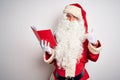 Middle age man wearing Santa Claus costume reading book over isolated white background doing happy thumbs up gesture with hand Royalty Free Stock Photo