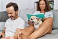 Middle age man and woman couple using laptop and reading book sitting on sofa with chihuahua at home Royalty Free Stock Photo