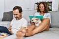 Middle age man and woman couple using laptop and reading book sitting on sofa with chihuahua at home Royalty Free Stock Photo