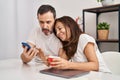 Middle age man and woman couple using smartphone drinking coffee sitting on table at home Royalty Free Stock Photo