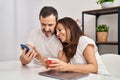 Middle age man and woman couple using smartphone drinking coffee sitting on table at home Royalty Free Stock Photo