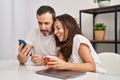 Middle age man and woman couple using smartphone drinking coffee sitting on table at home Royalty Free Stock Photo