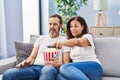 Middle age man and woman couple watching movie sitting on sofa at home Royalty Free Stock Photo