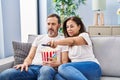 Middle age man and woman couple watching movie sitting on sofa at home Royalty Free Stock Photo