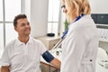 Middle age man and woman doctor and patient using tensiometer having medical consultation at clinic