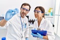 Middle age man and woman partners wearing scientist uniform analyzing sample at laboratory