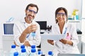 Middle age man and woman partners wearing scientist uniform reading document at laboratory
