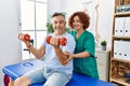 Middle age man and woman wearing physiotherapy uniform having rehab session using dumbbells at physiotherapy clinic