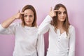 Middle age mother and young daughter standing over pink background pointing unhappy to pimple on forehead, ugly infection of